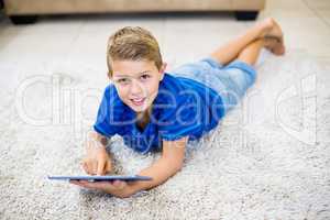 Portrait of boy lying on rug and using digital tablet