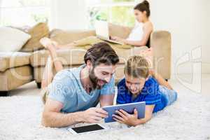 Father and son lying on rug and using digital tablet