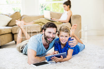 Portrait of father and son lying on rug and using digital tablet