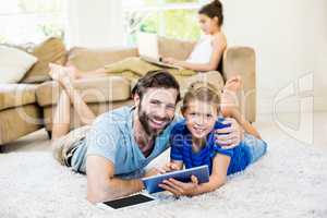 Portrait of father and son lying on rug and using digital tablet