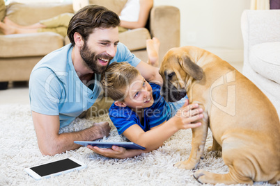 Father and son playing with a dog while using digital tablet