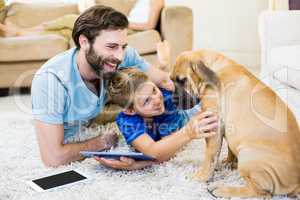 Father and son playing with a dog while using digital tablet