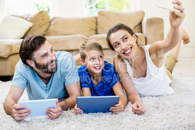 Parents and son lying on rug and taking selfie from phone