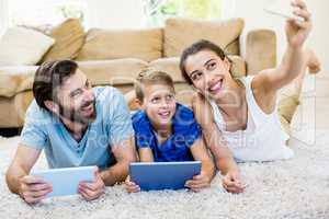 Parents and son lying on rug and taking selfie from phone