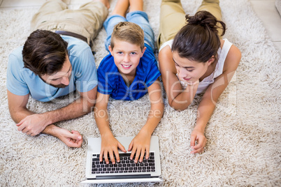 Parents and son lying on rug and using laptop