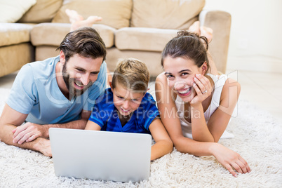 Parents and son lying on rug and using laptop