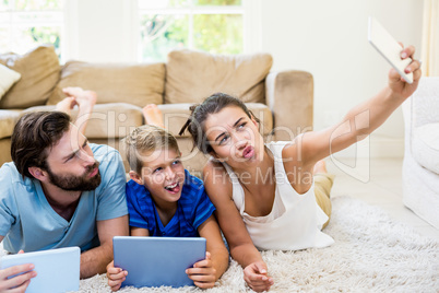 Parents and son lying on rug and taking selfie from phone