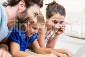 Parents and son lying on rug and using laptop