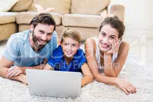 Portrait of parents and son lying on rug and using laptop