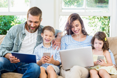 Family sitting on sofa and using a laptop, tablet and phone