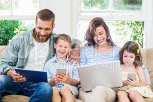 Family sitting on sofa and using a laptop, tablet and phone