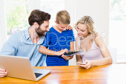 Parents and son using a laptop, tablet and phone