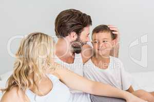 Parents and son sitting on bed in bedroom