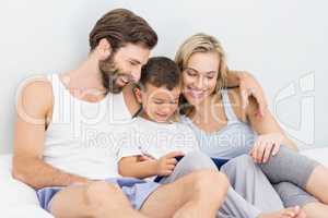 Parents and son sitting on bed and using digital tablet