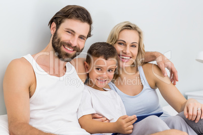 Portrait of parents and son sitting on bed and using digital tab