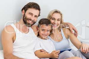 Portrait of parents and son sitting on bed and using digital tab