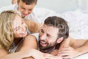 Parents and son lying on bed and having fun