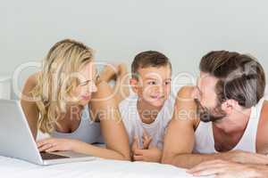 Parents and son lying on bed and using laptop