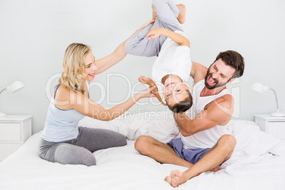 Parents and son sitting on bed and having fun in bedroom