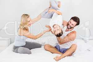 Parents and son sitting on bed and having fun in bedroom