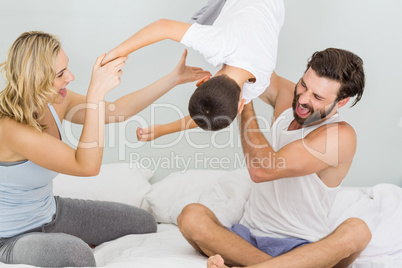 Parents and son sitting on bed and having fun in bedroom