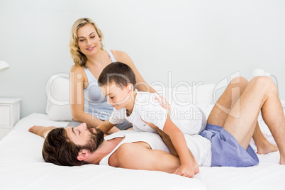 Parents and son having fun on bed in bedroom