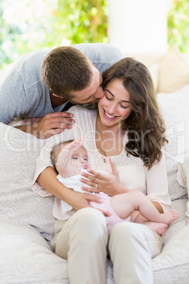 Woman kissing baby while man kissing her from behind