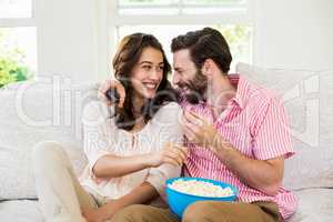 Happy couple sitting with a bowl of popcorn on sofa