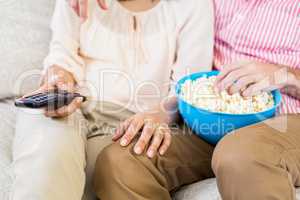 Mid section of couple sitting on sofa watching television