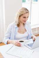 Woman holding a cup of coffee while using laptop