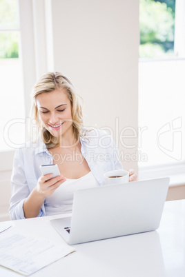 Woman text messaging on mobile phone while having cup of coffee