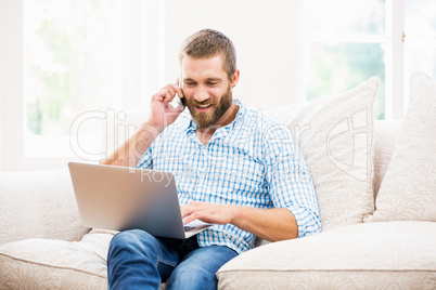 Man using laptop while talking on mobile phone in living room