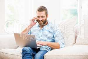 Man using laptop while talking on mobile phone in living room