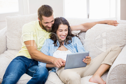 Couple sitting on sofa and using digital tablet in living room Couple sitting on sofa and using digital tablet in living room