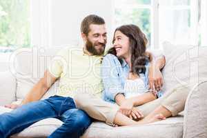 Young couple sitting on sofa with arm around