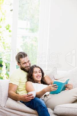 Man holding a cup of coffee while woman reading book