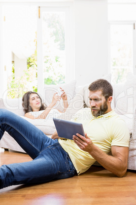 Couple using mobile phone and digital tablet in living room