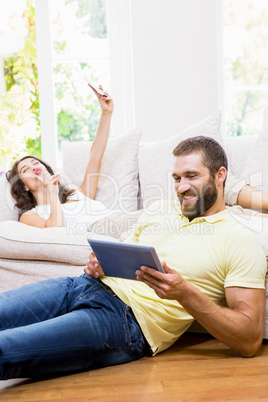 Man using digital tablet while woman taking selfie from mobile p