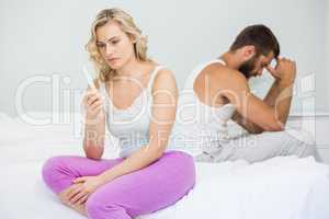 Worried woman looking at pregnancy test on bed