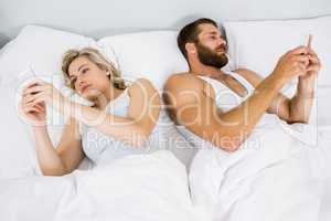 Couple using mobile phone on bed