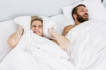 Woman covering ears while man snoring on bed