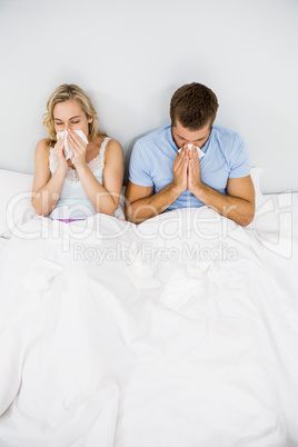 Couple covering nose while sneezing on bed