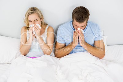 Couple covering nose while sneezing on bed