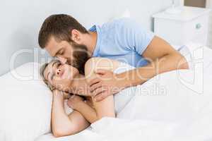 Man kissing woman on her cheek in bed