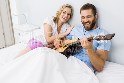 Man and woman playing guitar in bed