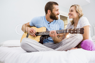 Man and woman playing guitar in bed