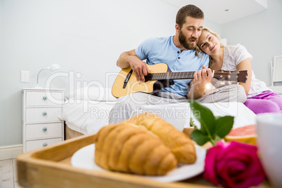 Man playing guitar for woman in bed