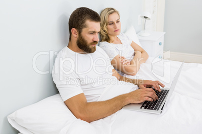 Woman watching man while using laptop in bed