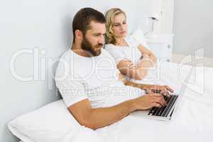 Woman watching man while using laptop in bed