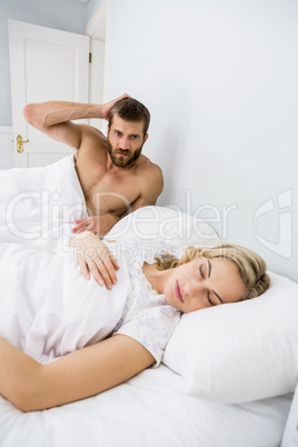 Aggressive man looking at woman sleeping in bed